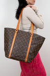 Person holding a Louis Vuitton monogram handbag against a plain background