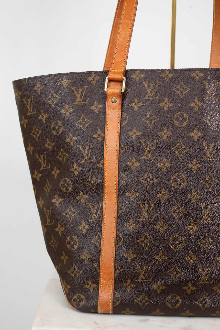 Louis Vuitton monogram handbag with brown leather straps on a white background