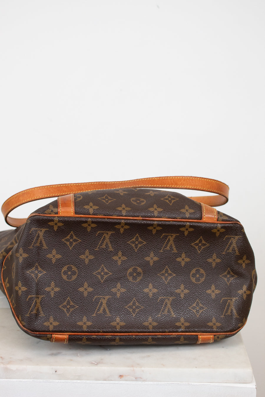 Brown monogram handbag with orange leather handles on a white background