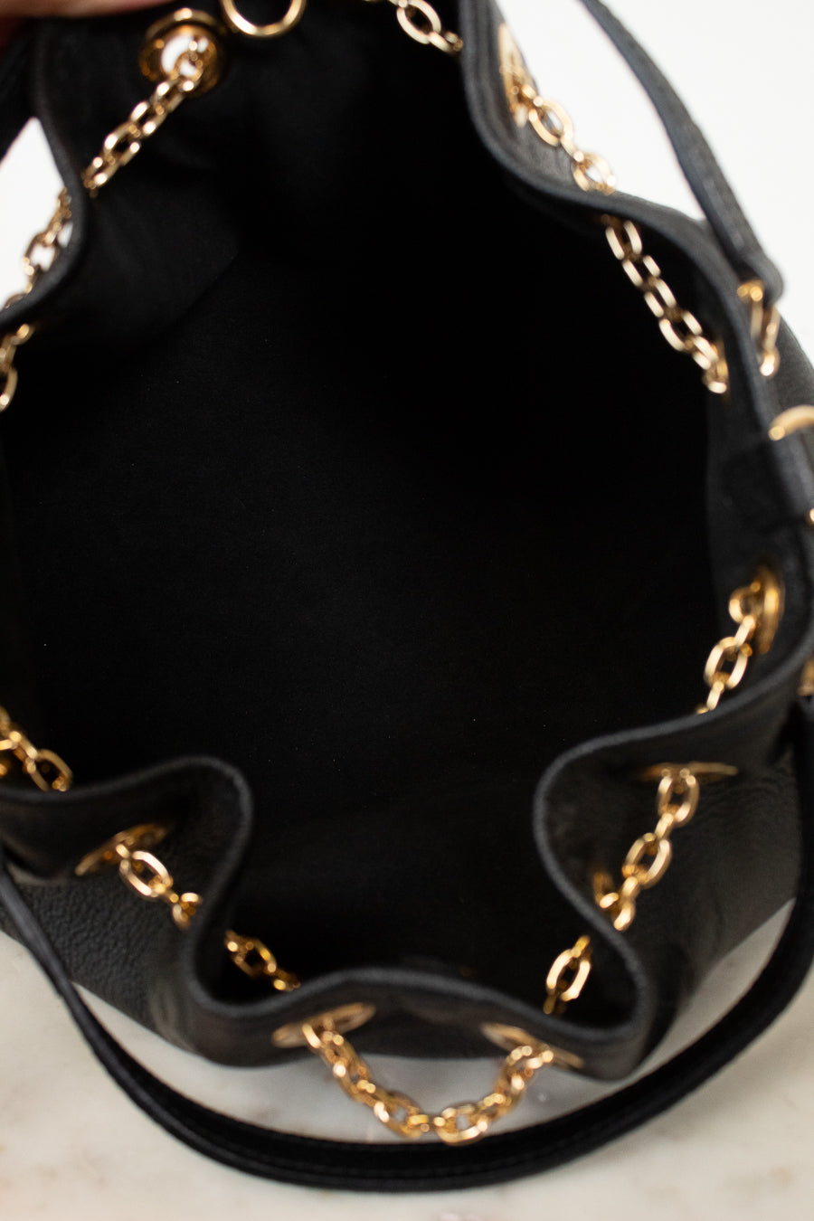 Close-up of the interior of a black leather bucket bag with gold-tone chain trim along the ruffled edge.