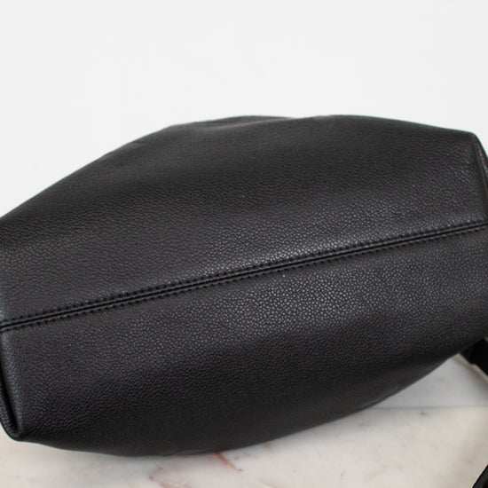 Bottom view of a black leather shoulder bag , resting on a white marble surface against a white background.
