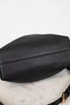 Bottom view of a black leather shoulder bag , resting on a white marble surface against a white background.