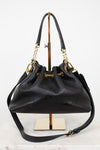 A black leather bucket bag with gold-tone hardware, displayed on a gold stand against a white background.