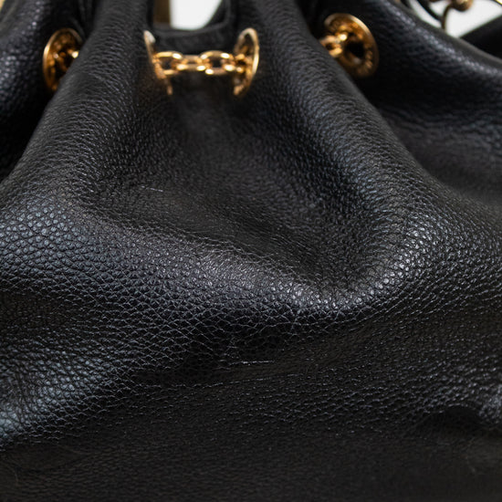 Close-up of a black leather drawstring chain bag with gold-tone chain and ring hardware, displayed on a stand.