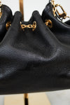 Close-up of a black leather drawstring chain bag with gold-tone chain and ring hardware, displayed on a stand.