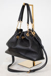 A black leather bucket bag with gold-tone hardware, displayed on a gold metal stand against a white background.