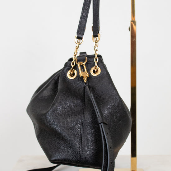 A black leather bucket bag with gold-tone hardware, displayed on a gold metal stand against a white background.