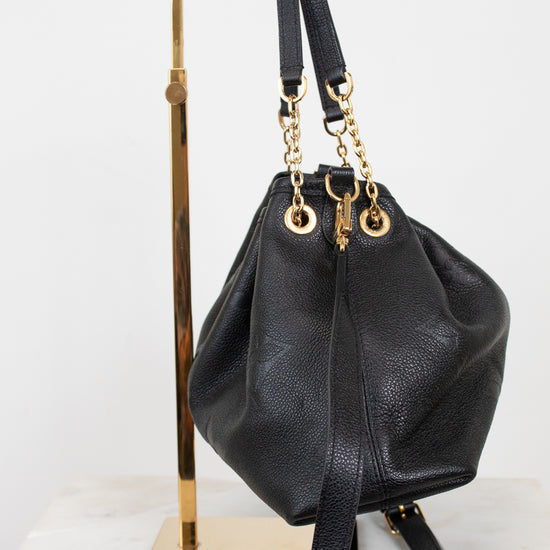 A black leather bucket bag with gold-tone hardware, displayed on a gold metal stand against a white background.