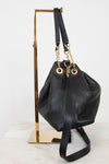 A black leather bucket bag with gold-tone hardware, displayed on a gold metal stand against a white background.