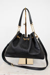 A black leather drawstring chain handbag with gold-tone hardware, displayed on a gold stand against a white background.