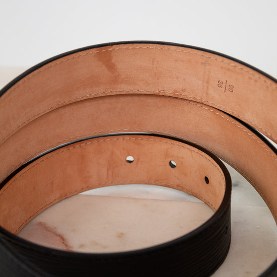Close-up of black leather belt with tan underside sitting on a white background.