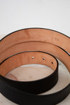 Close-up of black leather belt with tan underside sitting on a white background.