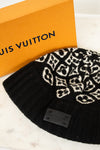Black beanie with white pattern next to a Louis Vuitton box on a marble surface