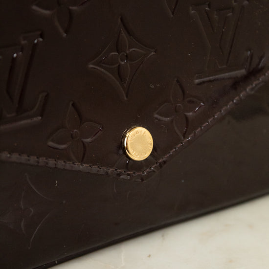 Close-up of a dark burgundy Louis Vuitton monogram leather bag with a gold-tone snap button, resting on a light marble surface.