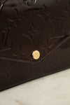Close-up of a dark burgundy Louis Vuitton monogram leather bag with a gold-tone snap button, resting on a light marble surface.
