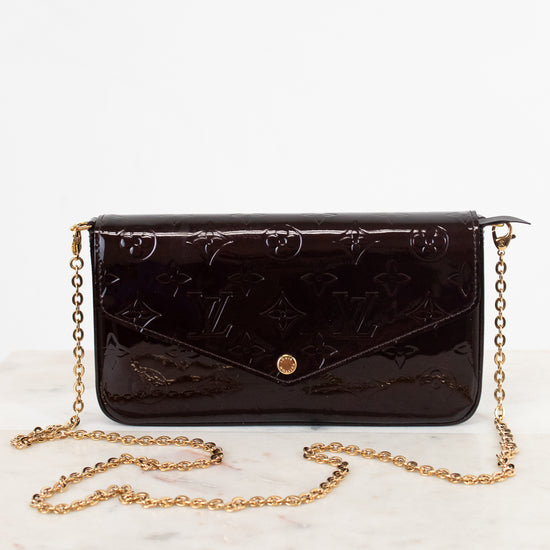 A dark burgundy patent leather clutch with a gold chain strap., isolated on a white background.