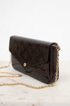 A dark brown Louis Vuitton monogram coated canvas clutch bag with a gold-tone chain strap, resting on a light marble surface against a white background.