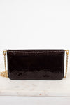 A dark burgundy Louis Vuitton patent leather clutch bag with an embossed monogram pattern and a gold chain strap, resting on a white marble surface against a white background.