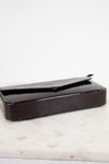 A dark burgundy glossy patent leather clutch bag with a textured flap, resting on a white marble surface against a white background.