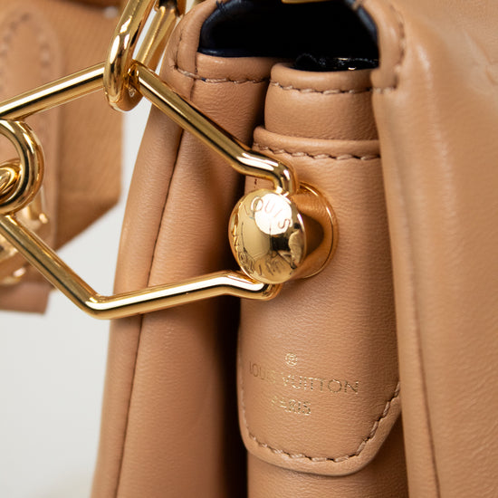 Close-up of a beige handbag with gold hardware on a light background