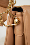 Close-up of a beige handbag with gold hardware on a light background