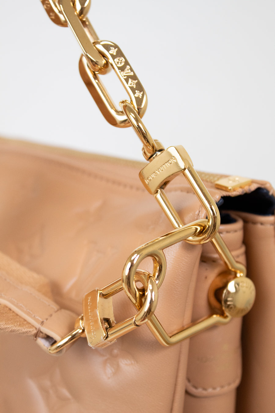 Close-up of a beige handbag with a gold chain handle on a light background