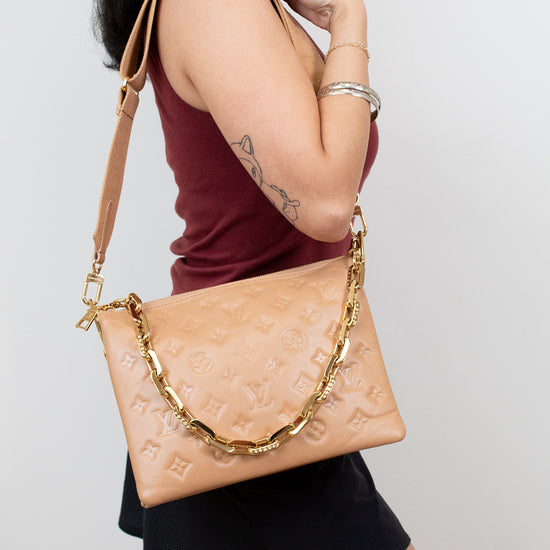 Woman carrying a beige handbag with a gold chain strap on a plain background