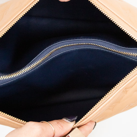 Close-up of a beige handbag with a gold zipper being held open by hands.