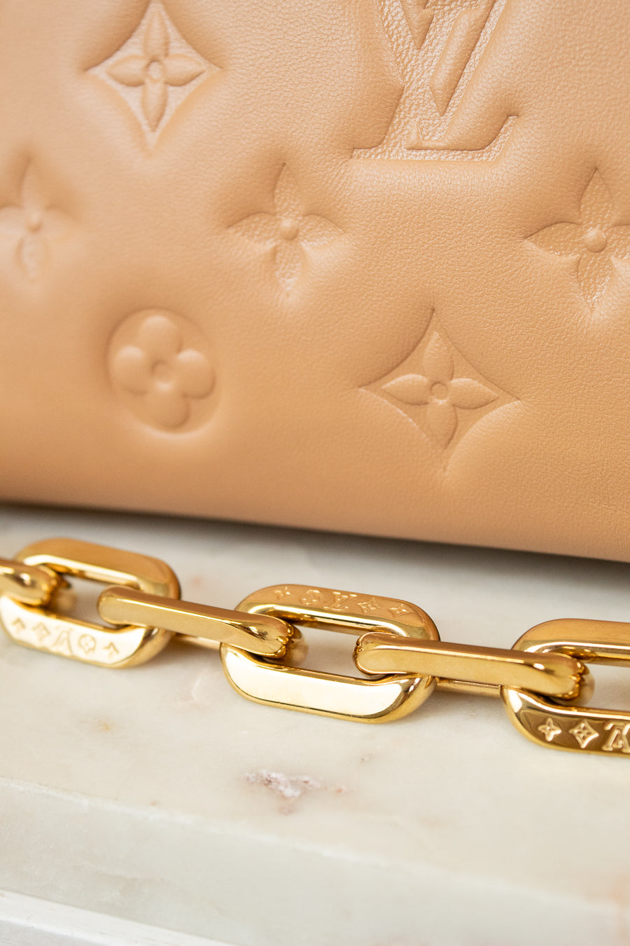 Close-up of a beige handbag with gold chain detail on a marble surface