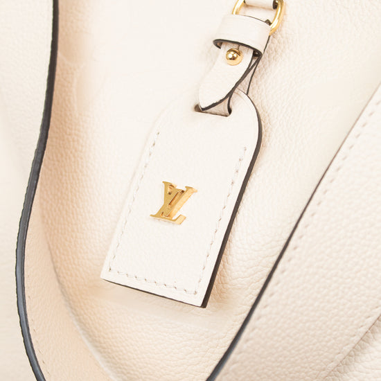 Close-up of a cream-colored leather Louis Vuitton shoulder bag with a matching leather luggage tag featuring a gold-tone LV logo, set against a light background.