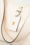 Close-up of a cream-colored leather Louis Vuitton shoulder bag with a matching leather luggage tag featuring a gold-tone LV logo, set against a light background.