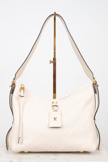 A cream-colored Louis Vuitton shoulder bag with gold-tone hardware and a matching leather hangtag, displayed on a stand against a white background.