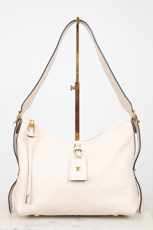 A cream-colored Louis Vuitton shoulder bag with gold-tone hardware and a matching leather hangtag, displayed on a stand against a white background.