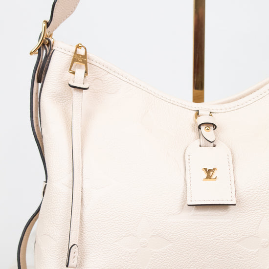 A close-up of a Louis Vuitton shoulder bag in off-white pebbled leather with gold-tone hardware and a matching leather hangtag featuring the LV logo.