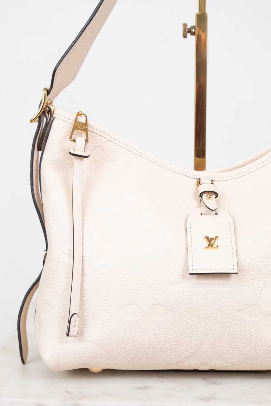 A close-up of a Louis Vuitton shoulder bag in off-white pebbled leather with gold-tone hardware and a matching leather hangtag featuring the LV logo.