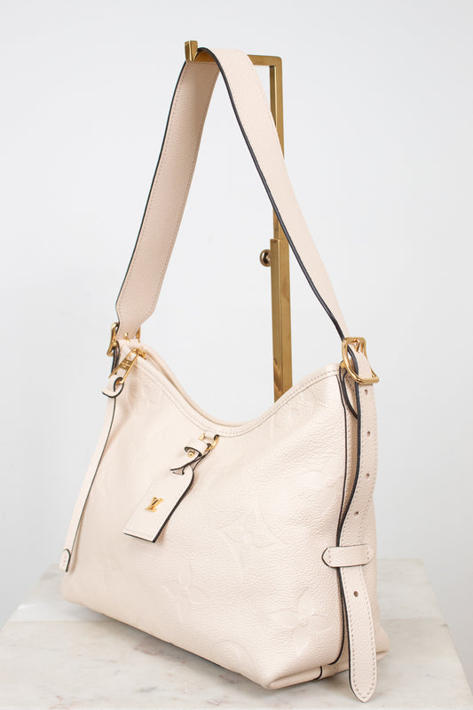 A cream-colored pebbled leather hobo shoulder bag with gold-tone hardware, displayed on a wooden stand against a light gray background.