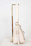 A light cream leather shoulder bag with gold-tone hardware, displayed on a minimalist gold metal stand against a clean white background.