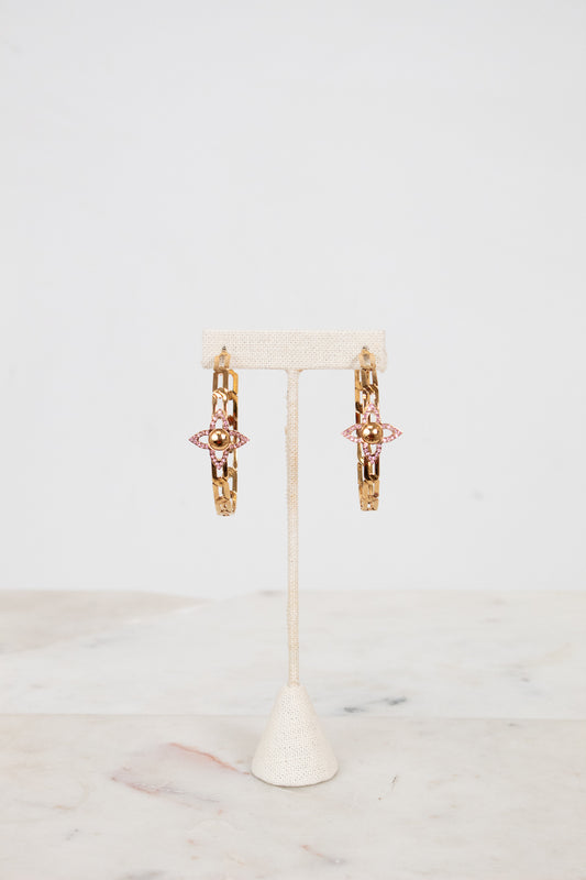 Gold hoop earrings with pink accents on a white stand with a white background