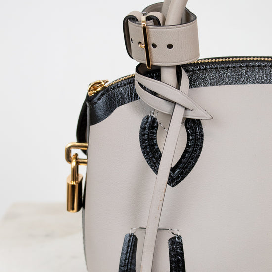 White handbag with black accents and gold hardware on a light gray background