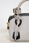 White handbag with black accents and gold hardware on a light gray background