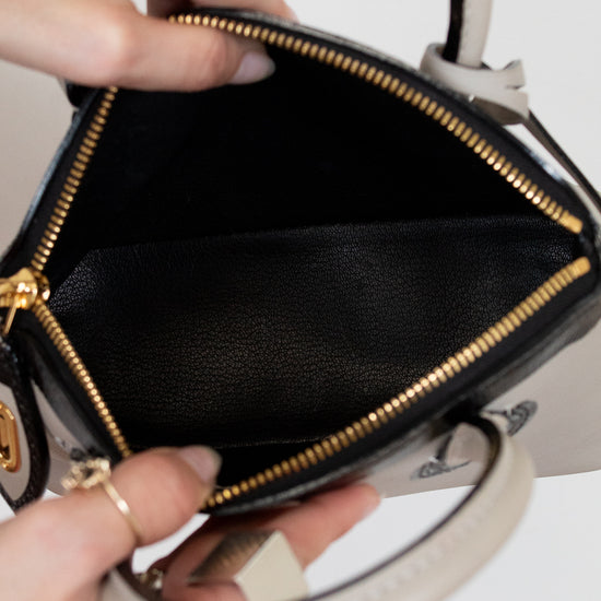 Black handbag with gold zipper held by a person on a white background