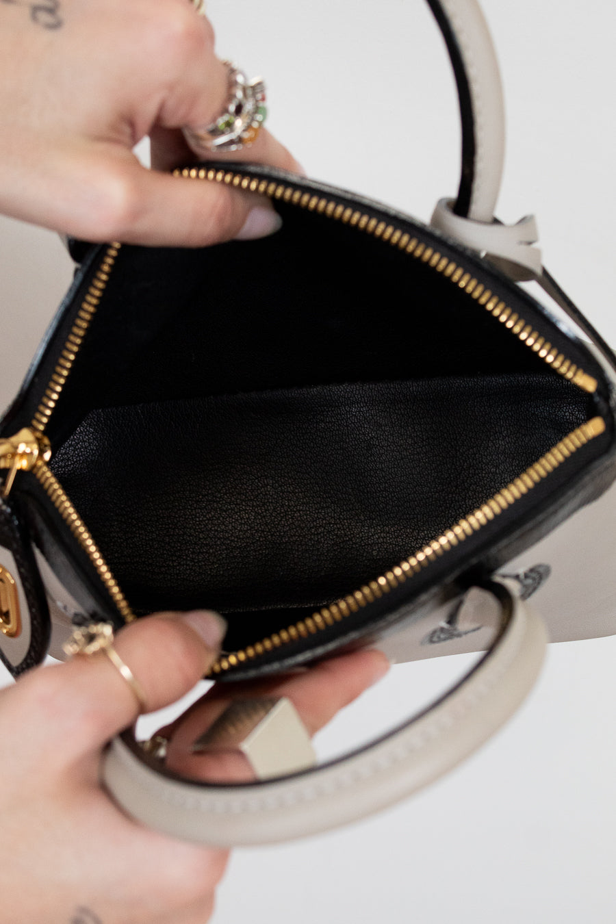 Black handbag with gold zipper held by a person on a white background