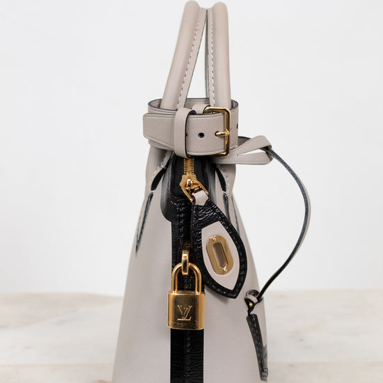 Silver handbag with black strap and gold lock on a white background