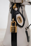 Close-up of a white handbag with a gold padlock on a light gray background
