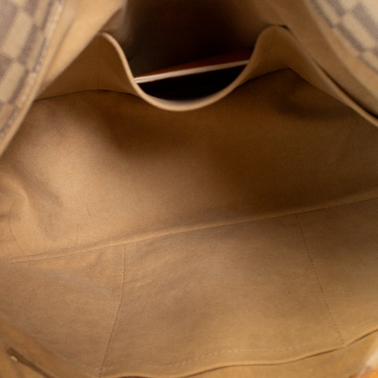 Close-up view of the interior of a handbag, showing a beige fabric lining, a top pocket, and part of the patterned exterior near the opening.