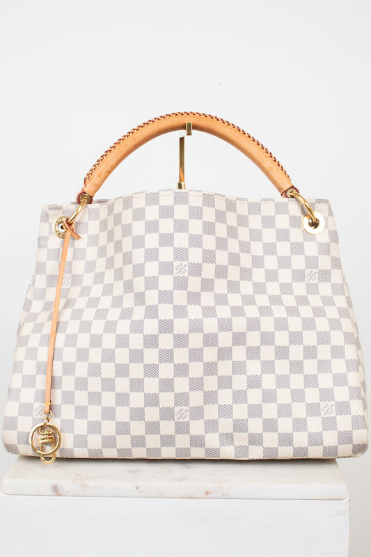 A Louis Vuitton handbag in Damier Azur coated canvas, featuring a light gray and white checkered pattern, a tan leather top handle, and gold-tone hardware.