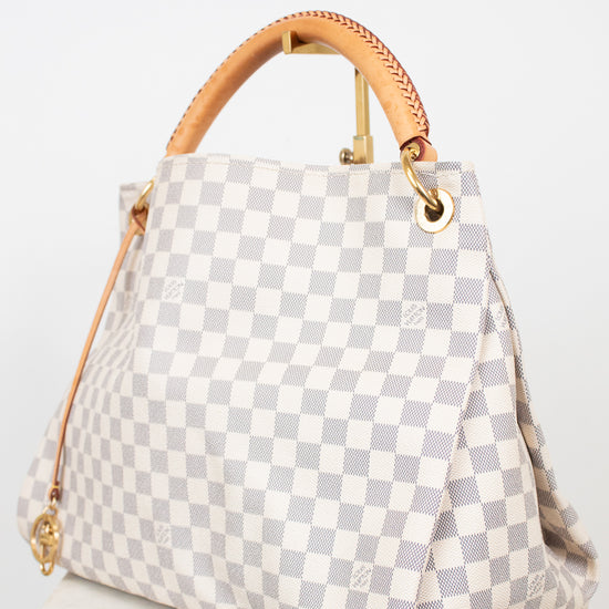 A Louis Vuitton Damier Azur canvas handbag with a light gray and white checkered pattern, tan leather top handles, and gold-tone hardware, displayed on a white marble surface against a white background.