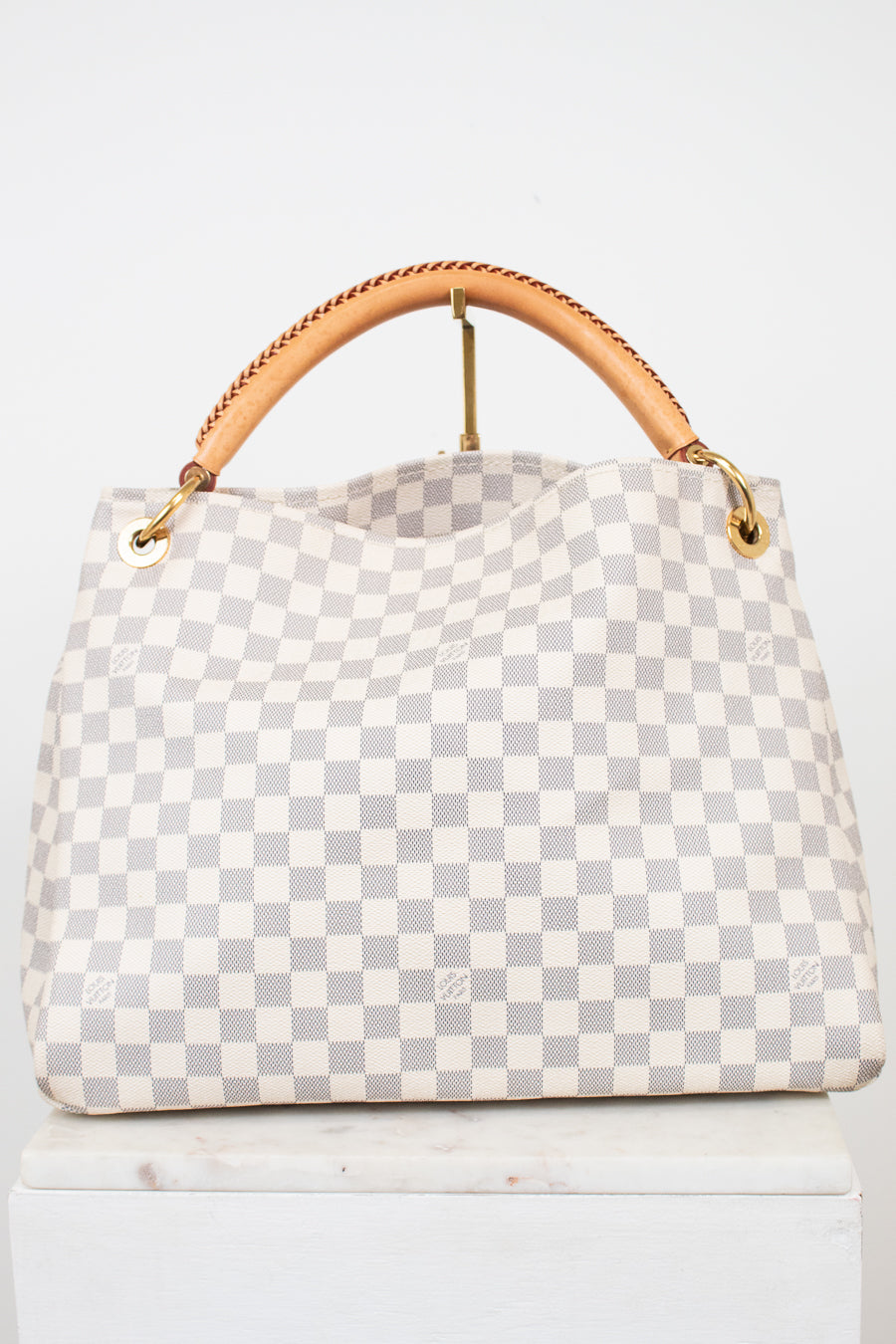 A light gray and white checkered handbag with a tan leather top handle and gold-tone hardware, displayed on a white surface against a white background.