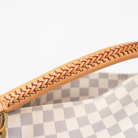 Close-up of a handbag handle made of light tan leather with a braided stitch pattern, attached to a gray and white checkered canvas body.