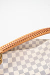 Close-up of a handbag handle made of light tan leather with a braided stitch pattern, attached to a gray and white checkered canvas body.